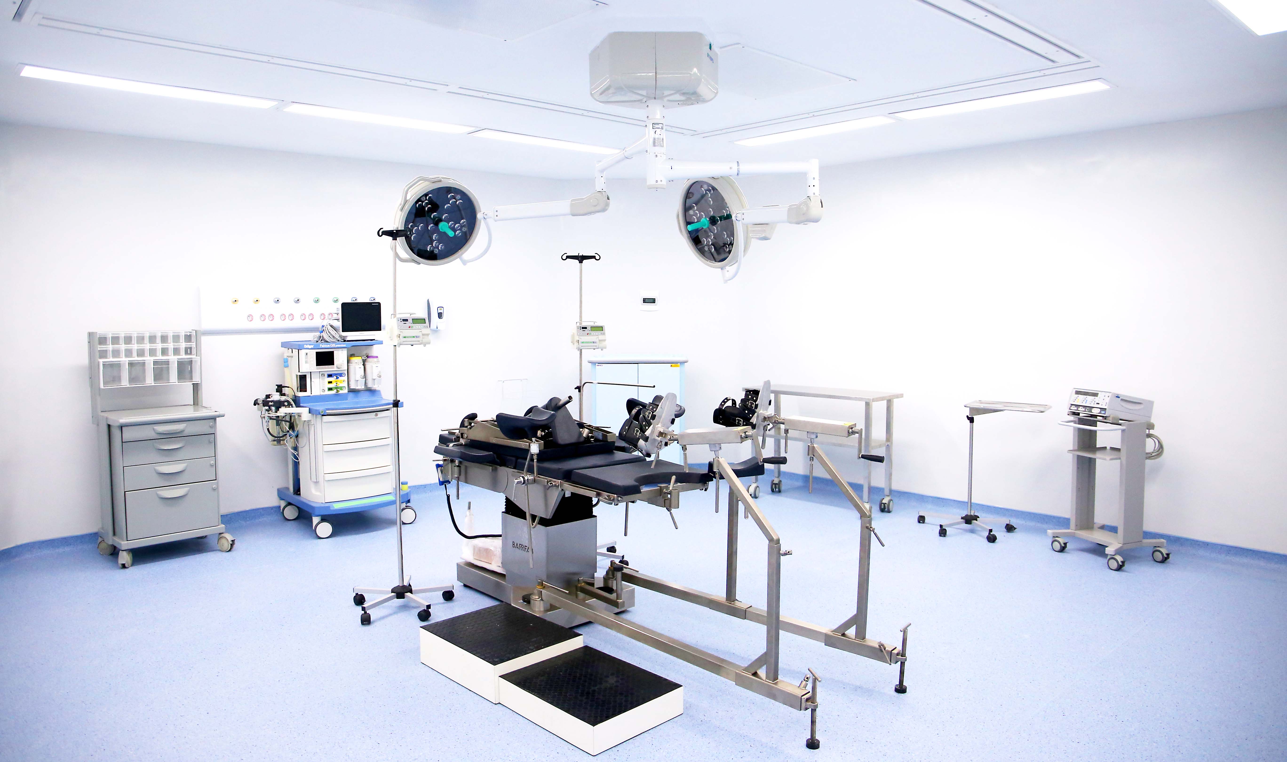 Sala de cirurgia com maca ao meio e equipamentos ao redor